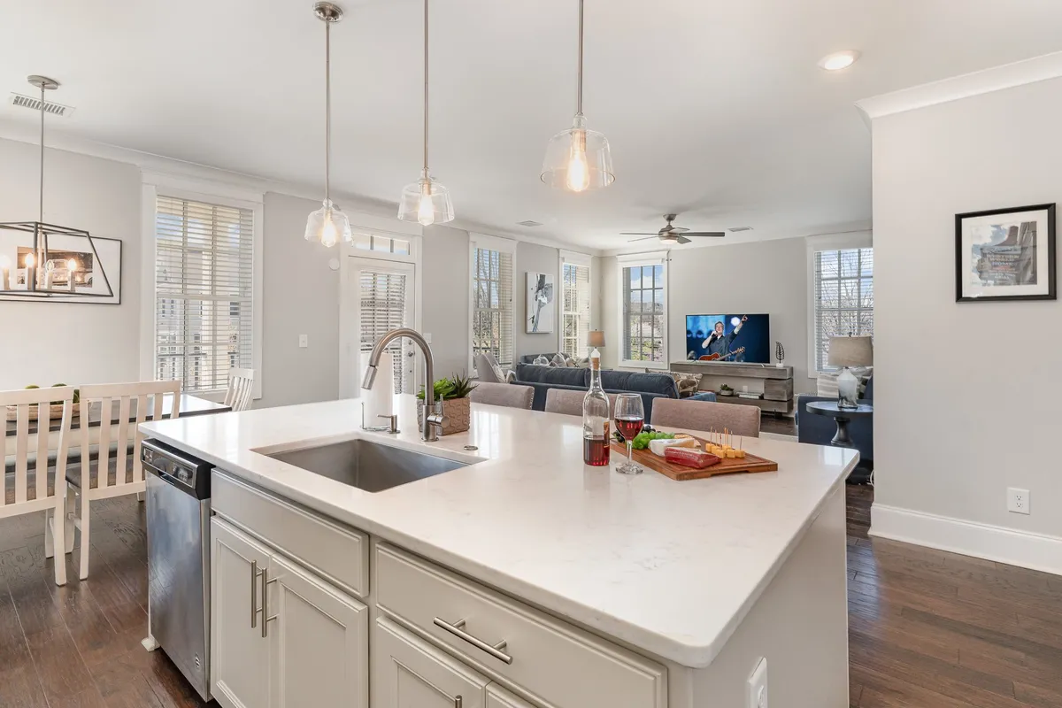 This image captures a seamless open-concept space featuring the kitchen island, dining table, living room sofa, and a television, all bathed in natural light from large windows. The layout shows the fluid connection between the kitchen, dining, and living areas, emphasizing the shared, social nature of the penthouse's main gathering space.