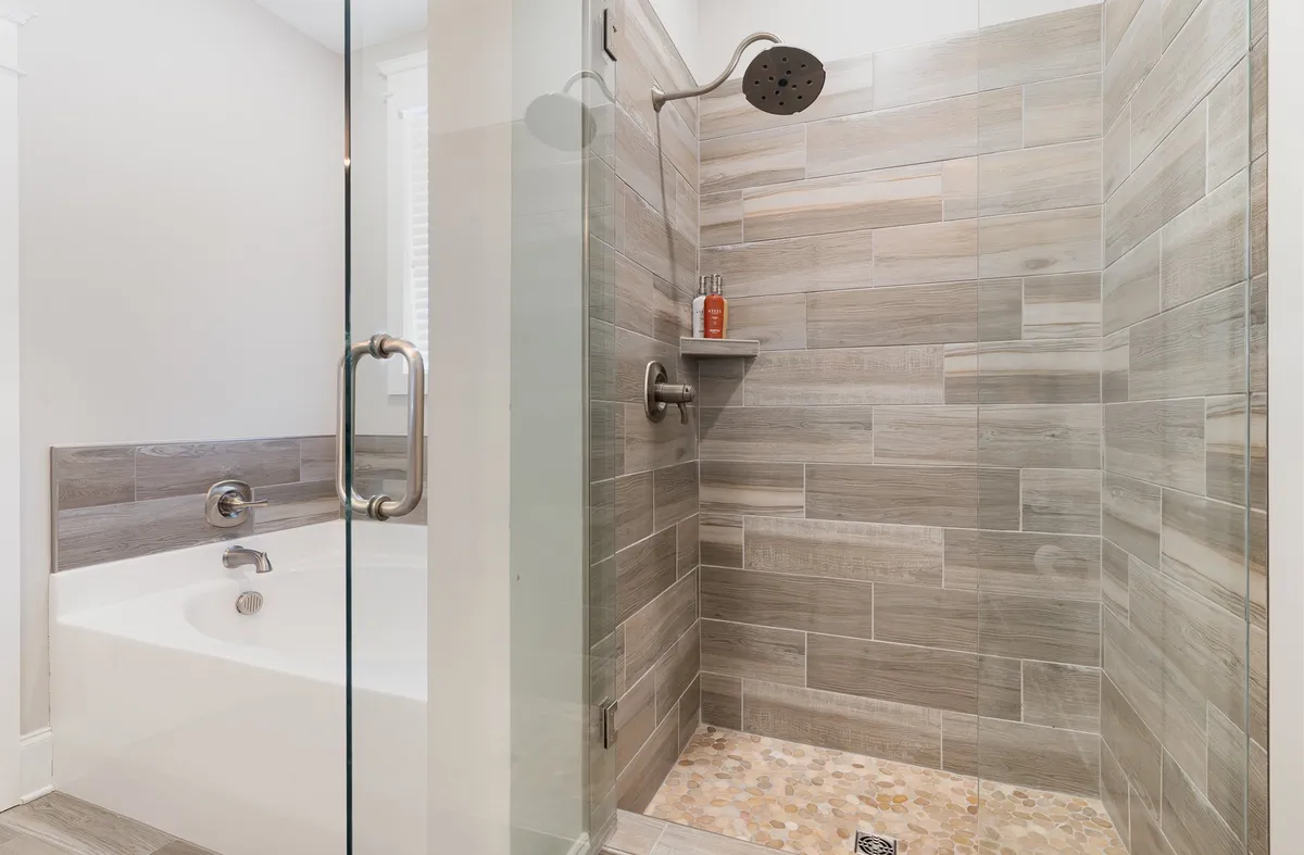 A spa-like bathroom featuring a glass shower enclosure, a freestanding bathtub, and textured tile walls. The serene atmosphere is complemented by soft lighting and a sense of tranquility, evoking the feel of a luxury spa retreat.
