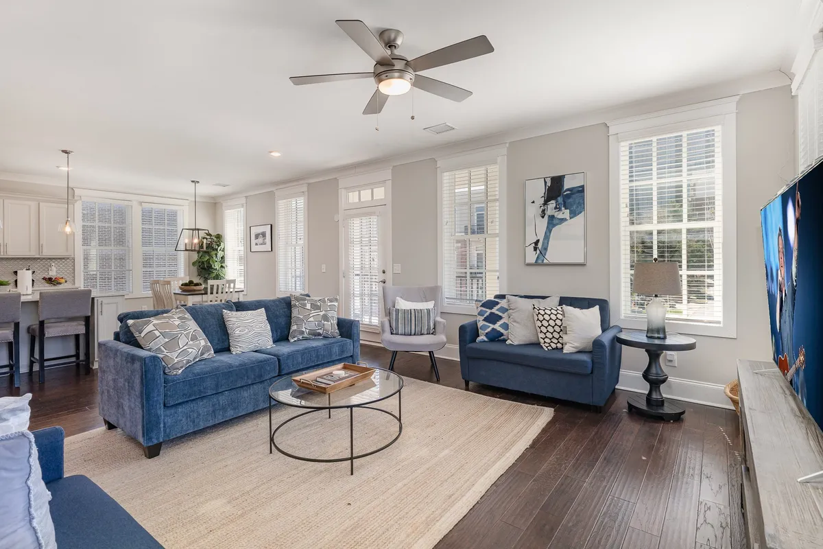 A comfortable, stylish living room with blue sofas, a round coffee table, artwork, and a prominent television. The layout encourages lounging, entertainment, and social interaction, evoking the spirit of cozy movie nights or game days with friends.