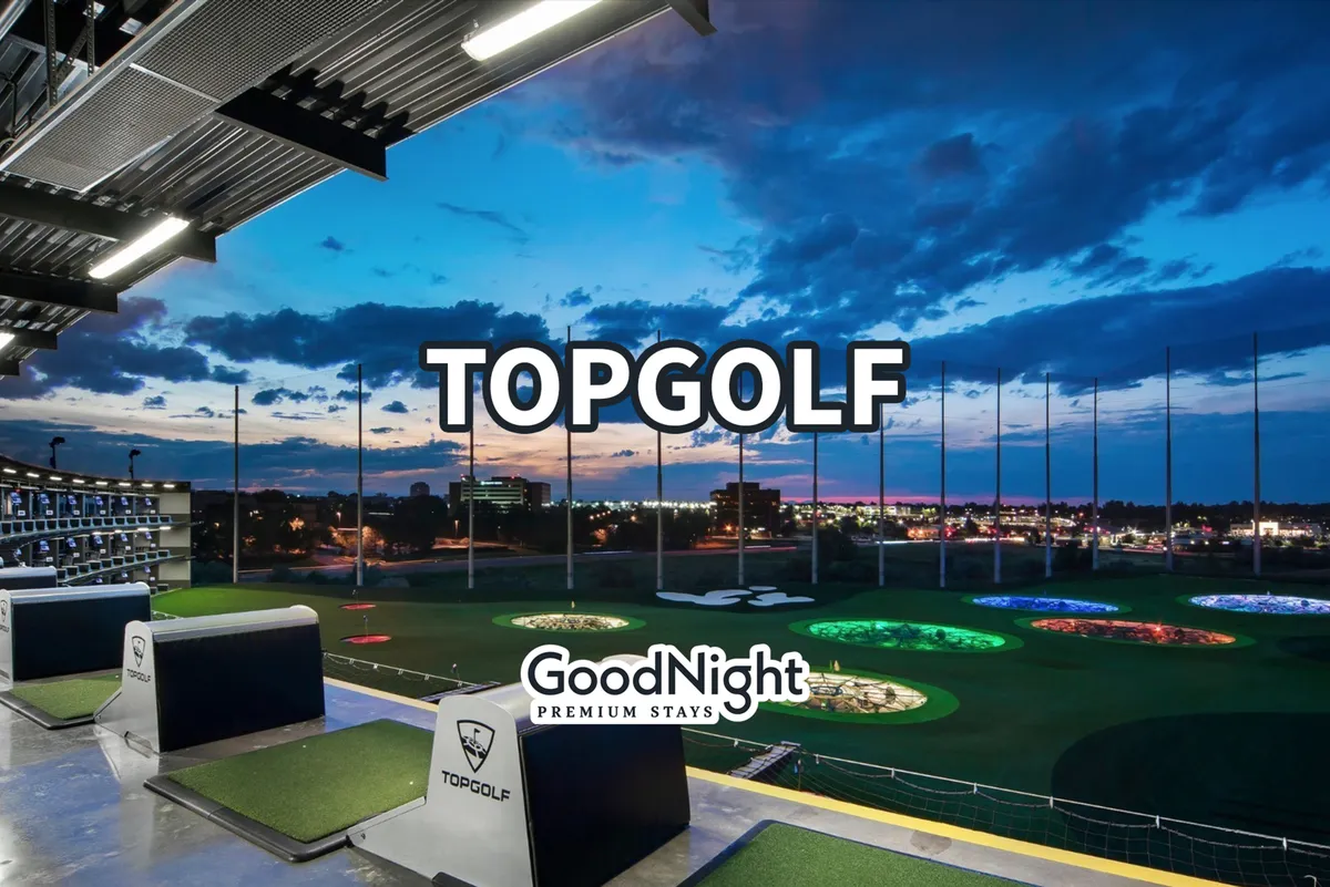 The photo presents the vibrant driving ranges of Topgolf, with colorful target areas and a view of the city skyline in the background. The energetic, social atmosphere is clear, suggesting a blend of work and leisure.