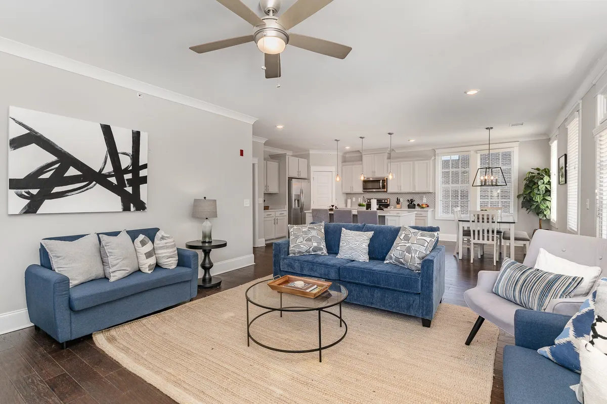 A spacious living room with blue sofas, a central coffee table, and abstract wall art. The arrangement is ideal for socializing or relaxing, and the mood is inviting and communal, echoing the idea of the living room as a flexible sleeping and gathering space.