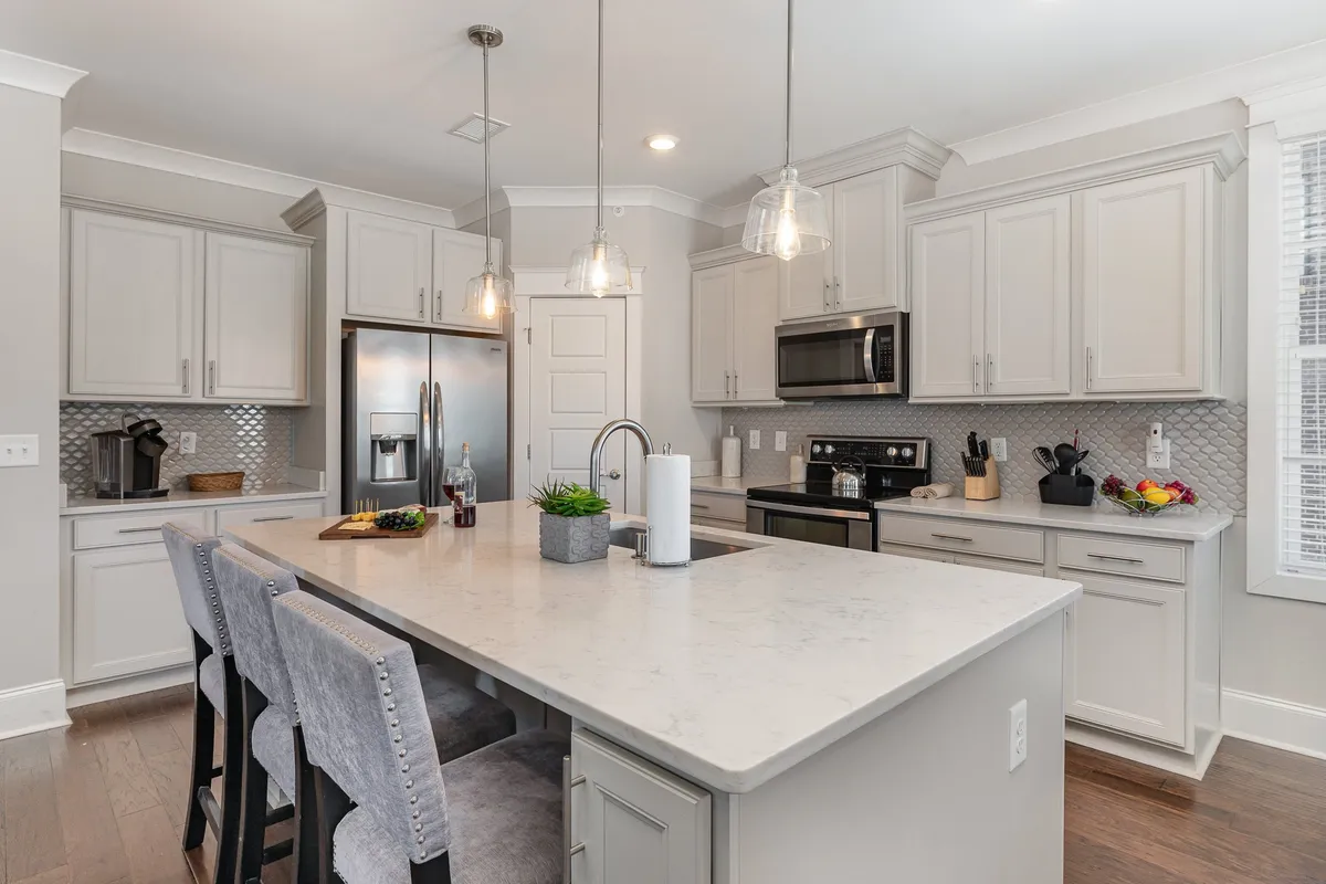 A stylish contemporary kitchen with a spacious island, stainless steel appliances, pendant lighting, and a striking hexagonal backsplash. The design exudes modern elegance, and the island is poised for food prep, casual meals, or socializing.